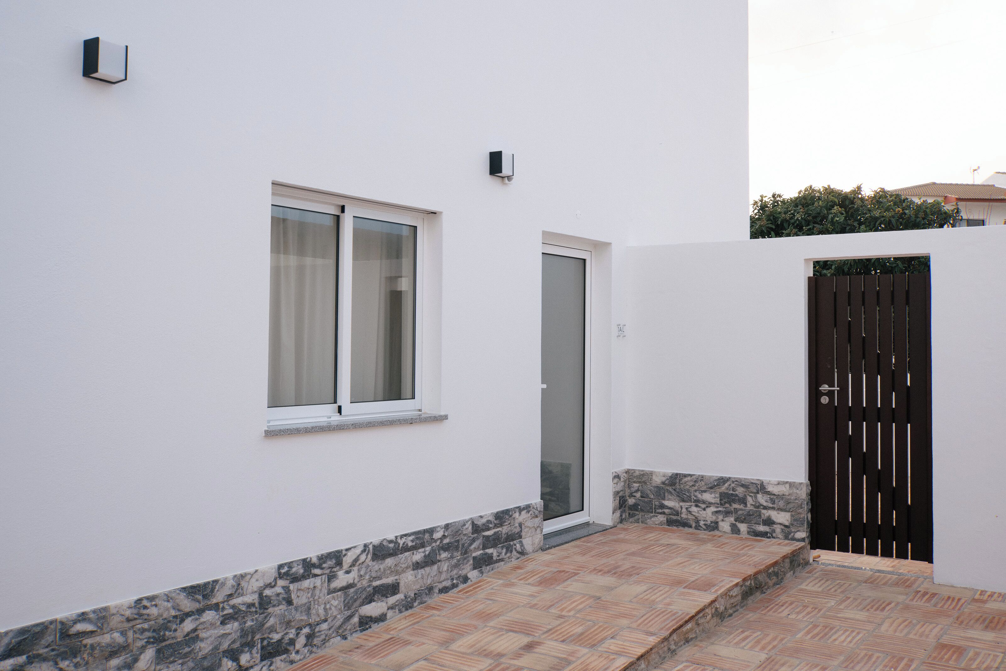 Un edificio moderno con fachada blanca, entrada de baldosas y portón negro.