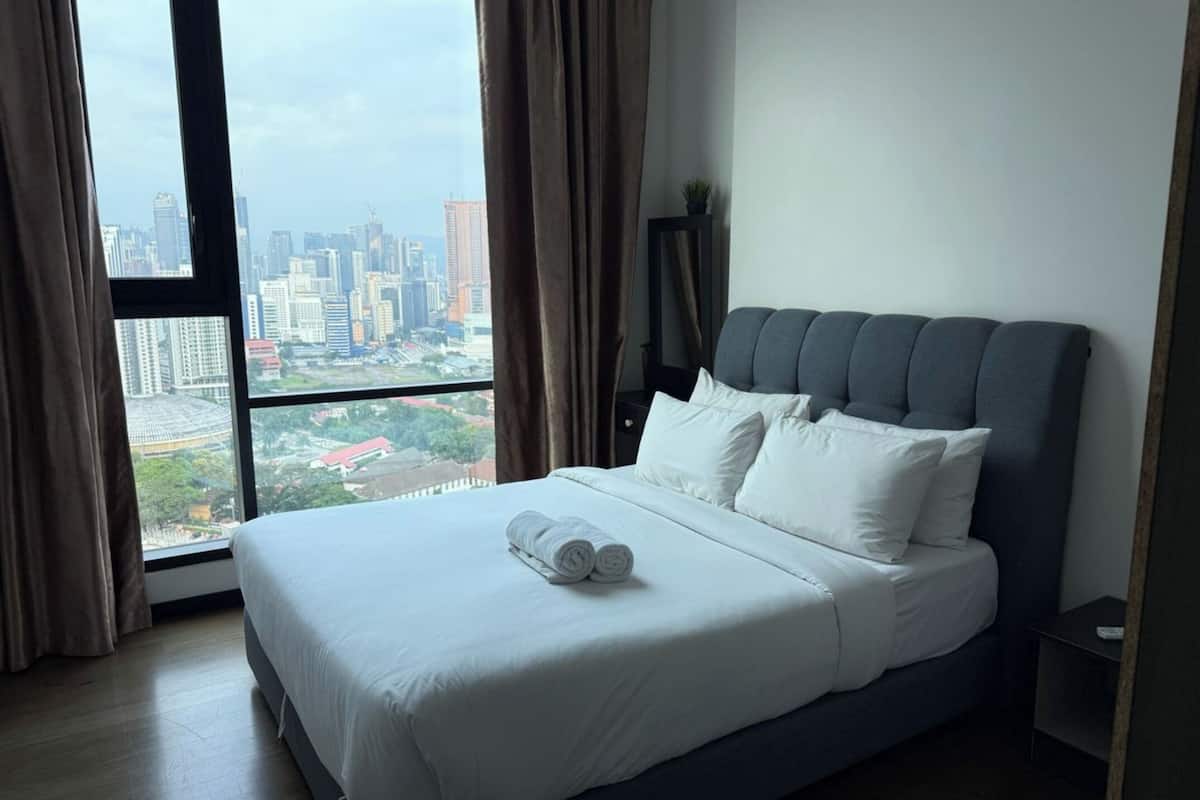 Een hotelkamer met een groot bed, een nachtkastje en uitzicht op een stadsbeeld door een groot raam.