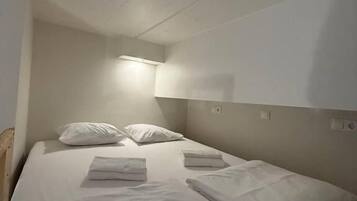 Una cama individual con ropa de cama y almohadas blancas, una mesita de noche y una lámpara de pared.