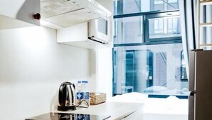 A modern kitchen with a microwave, kettle, and coffee maker on the counter, a window with a view of buildings, and a refrigerator. - Cozy Suites (Tallinn)