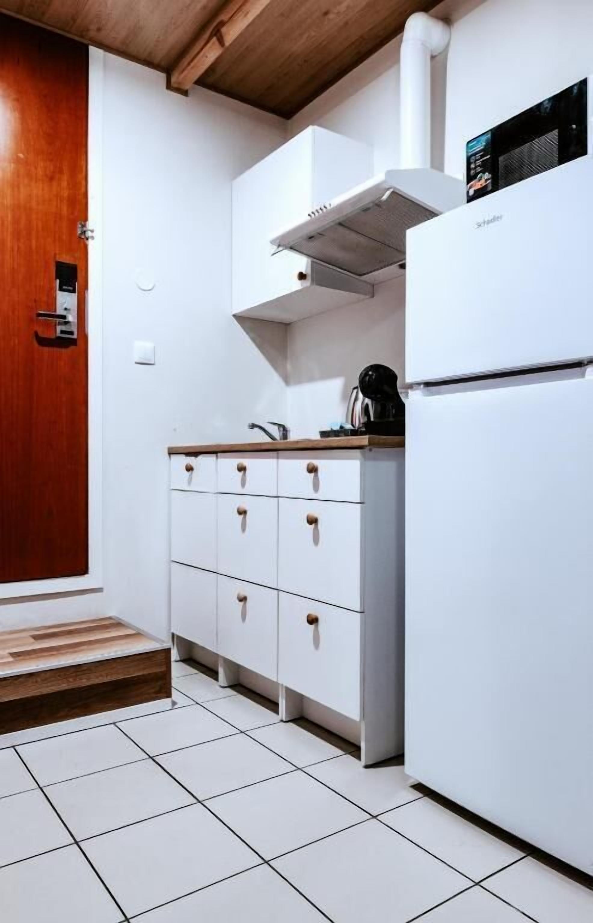 Una cocina con armarios blancos, una puerta de madera y un refrigerador blanco.