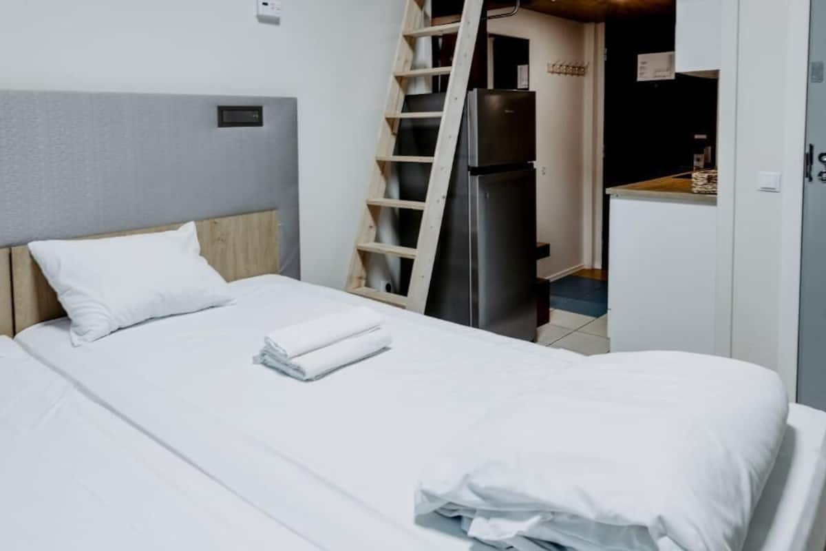 A hotel room with a bed, a wardrobe, a refrigerator, and a wooden ladder.