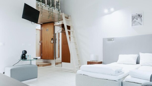 A modern hotel room with a bed, bedside table, and a TV mounted on the wall. - Cozy Suites (Tallinn)