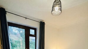 A bedroom with a bed, a bedside table with a lamp, a window with curtains, and a door.