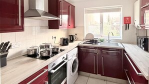 A modern kitchen with red cabinets, a built-in oven, a washing machine, and a window providing natural light.