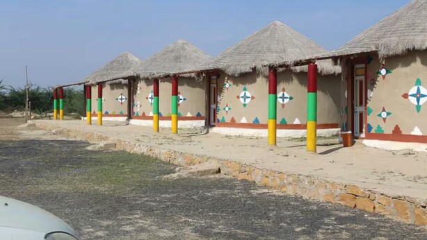 A row of thatched-roof huts with colorful pillars and geometric wall decorations. - Rann Roshni Homestay – Family Friendly Stay in Kutch 6 (Bhirandiara)