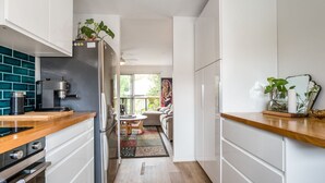 Et moderne køkken med kaffemaskine, køleskab og spiseområde med sofa og bord.