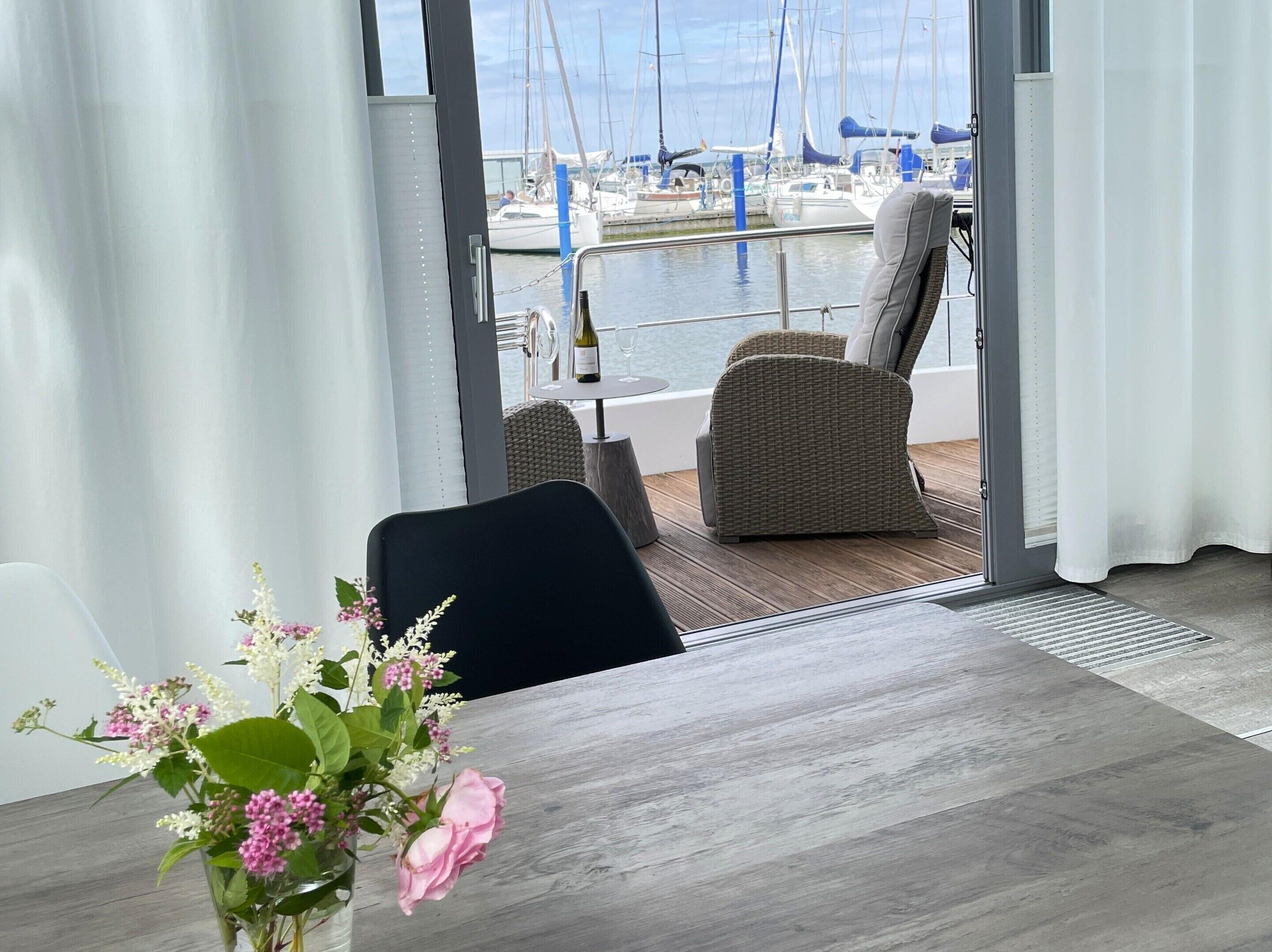 Een eetruimte met uitzicht op een jachthaven, een tafel met een bloevas en een stoel.