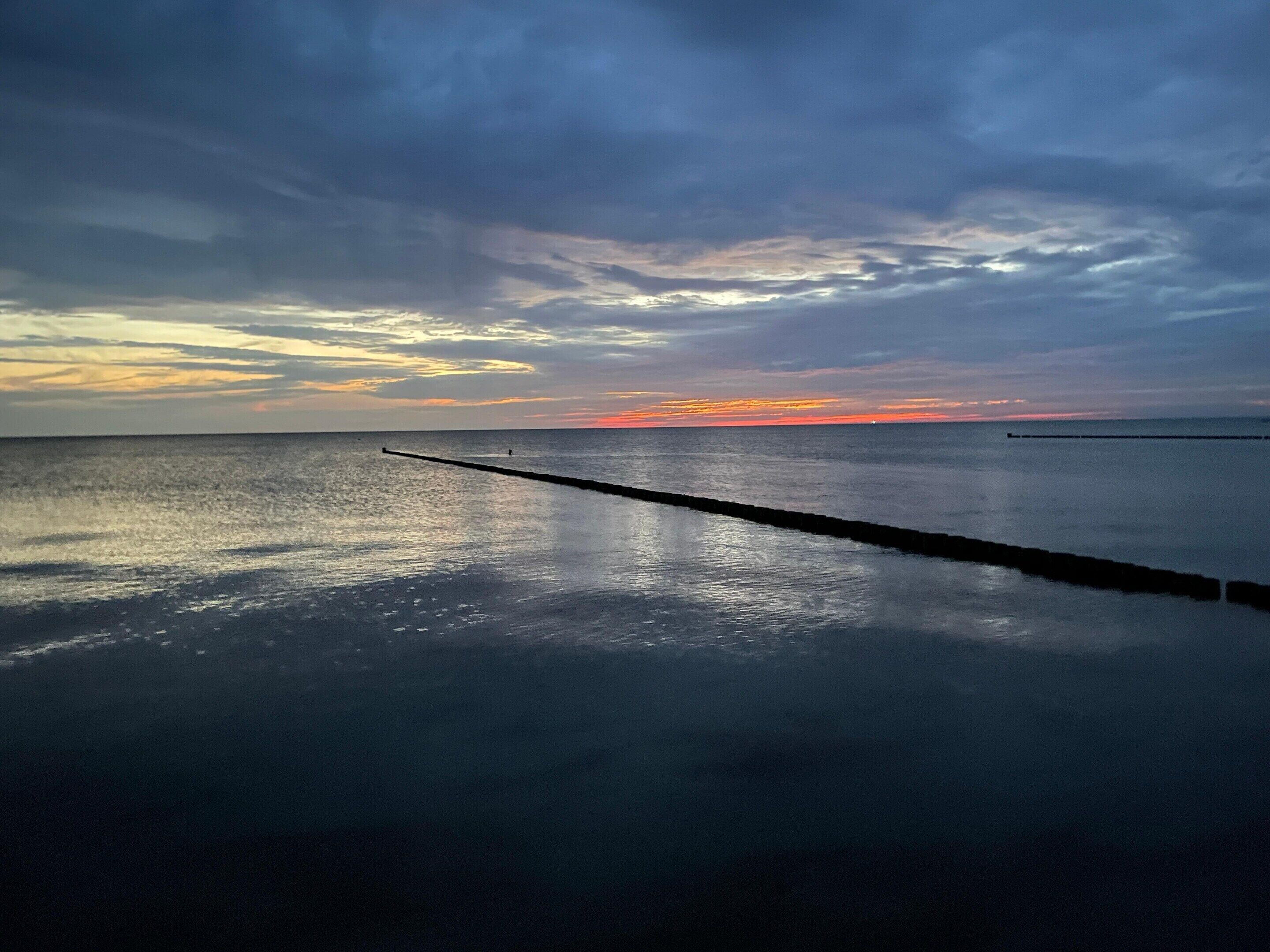 Un mar tranquilo al atardecer con un muelle de madera que se adentra en el agua.