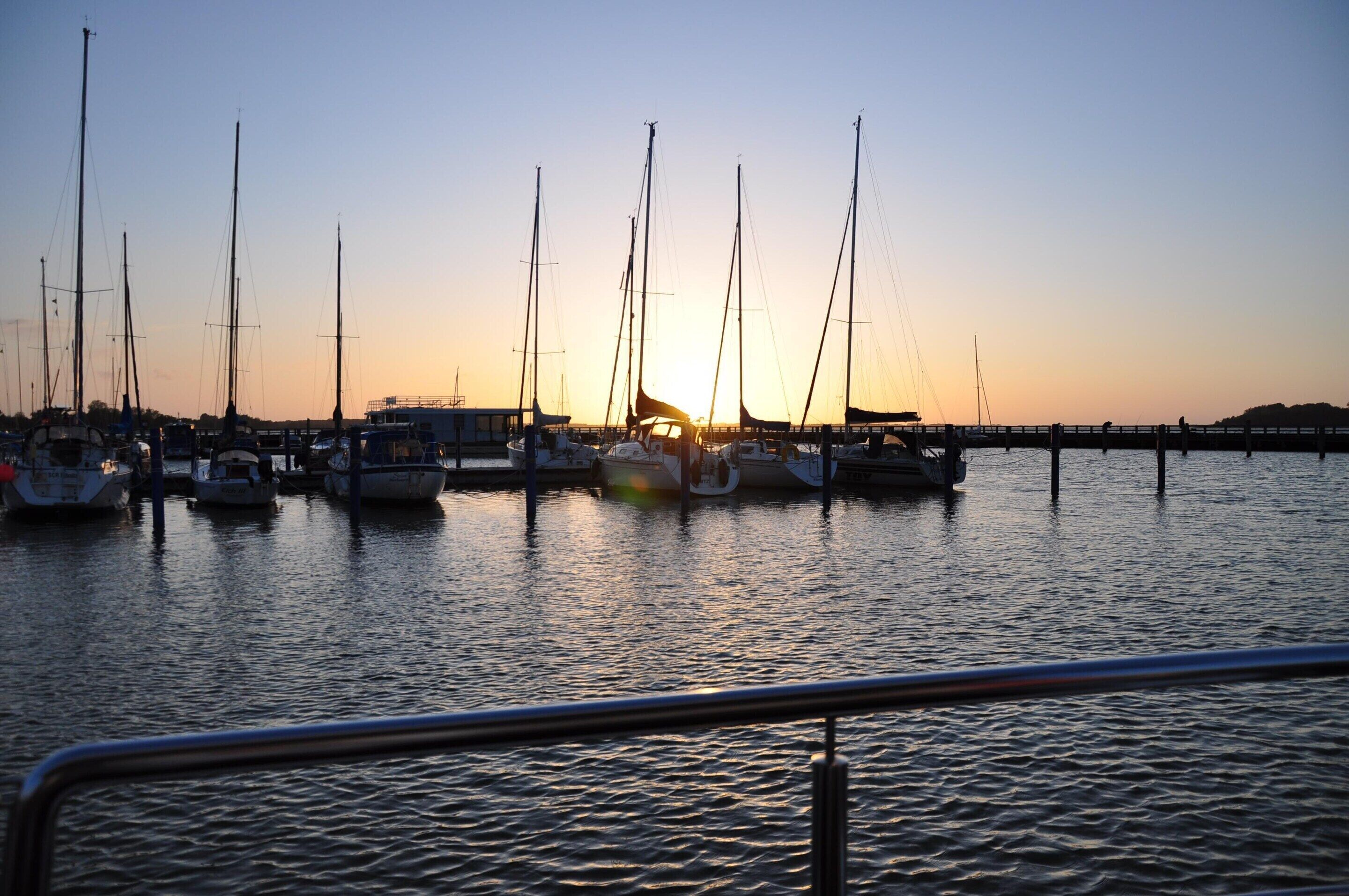 Un port de plaisance où sont amarrés de nombreux voiliers, au coucher du soleil.