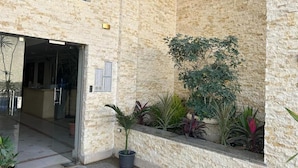 A building entrance with a stone facade, a potted plant, and a small garden area. - شقة ألترا سوبر لوكس بكمبوند البارون المعادى (Cairo Governorate)