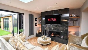 Ein modernes Wohnzimmer mit Kamin, einem flachbildfernseher, der an einer Marmorwand montiert ist, und einer gemütlichen Sitzecke mit Sofa und Ottoman.