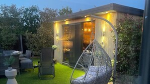 Eine moderne Terrassenanlage mit Hängesessel, Essbereich mit Korbmöbeln und gepflegtem Rasen.