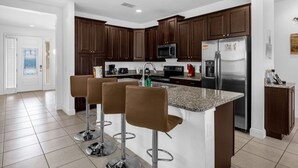 Une cuisine moderne avec des meubles en bois foncé, des appareils électroménagers en acier inoxydable et un îlot central doté de tabourets de bar.
