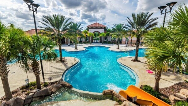 A swimming pool with multiple lanes, surrounded by palm trees and a building with a red-tiled roof. - 25% Off 5BR Resort Pool/Lazy river/Slides/Gym (Davenport)