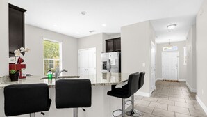 A modern kitchen with a central island, bar stools, and a refrigerator. - 25% Off 5BR Resort Pool/Lazy river/Slides/Gym (Davenport)