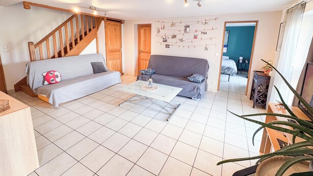 A living room with a staircase, two sofas, a coffee table, and a wall decorated with pictures. - Quiet country & family gîte 20min from Caen (Cintheaux)