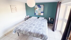A bedroom with a bed, a nightstand, a wall clock, a framed picture, and a window with curtains. - Quiet country & family gîte 20min from Caen (Cintheaux)