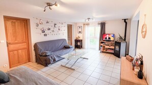 A living room with a sofa, a coffee table, a TV, and a bookshelf. - Quiet country & family gîte 20min from Caen (Cintheaux)