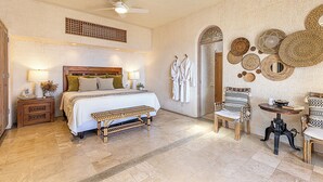 A spacious bedroom with a large bed, a wooden nightstand, a bench, two chairs, a small table, and a ceiling fan. - Casa Dos Hermanas by Wynwood House (Cabo San Lucas)