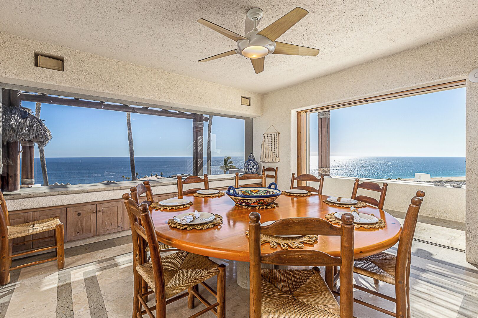 A dining area with a view of the ocean, wooden furniture, and a ceiling fan.