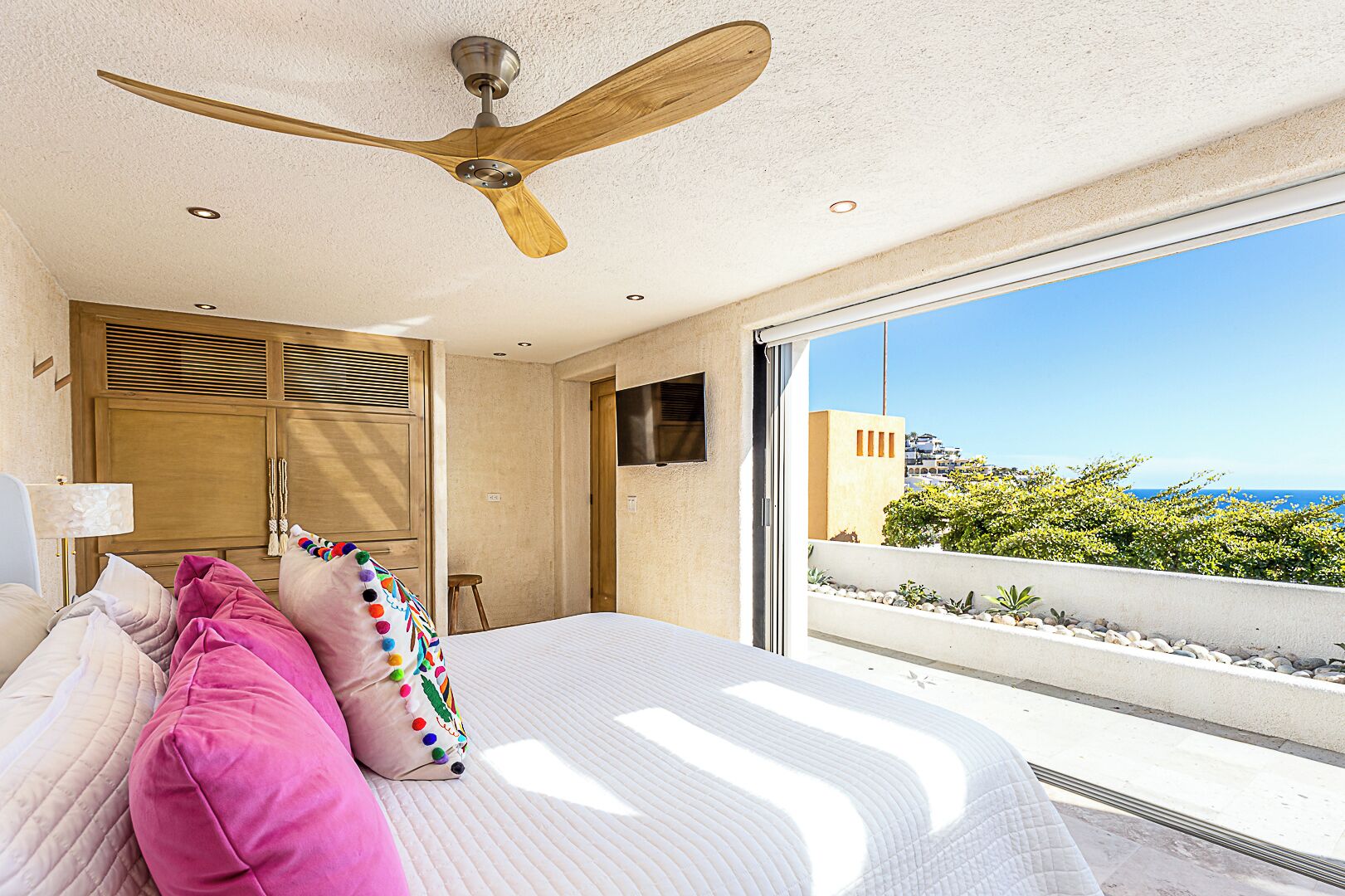 A bedroom with a large bed, a ceiling fan, a TV, and a view of the ocean.