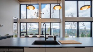 A modern kitchen with large windows, a central island, and pendant lighting. - Spa, Views & Nature | Panoraama Finlandais (Saint-Côme)