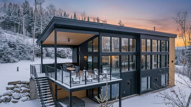 A modern, two-story house with a glass balcony, surrounded by a snowy landscape. - Spa, Views & Nature | Panoraama Finlandais (Saint-Côme)