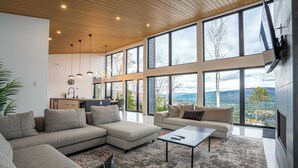 A spacious living room with large windows, a sectional sofa, a coffee table, and a view of the outdoors. - Spa, Views & Nature | Panoraama Finlandais (Saint-Côme)
