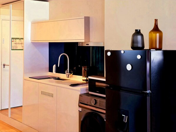 A compact kitchen with a sink, a stove, a microwave, and a refrigerator. - Q'ure Batumi (Batumi)