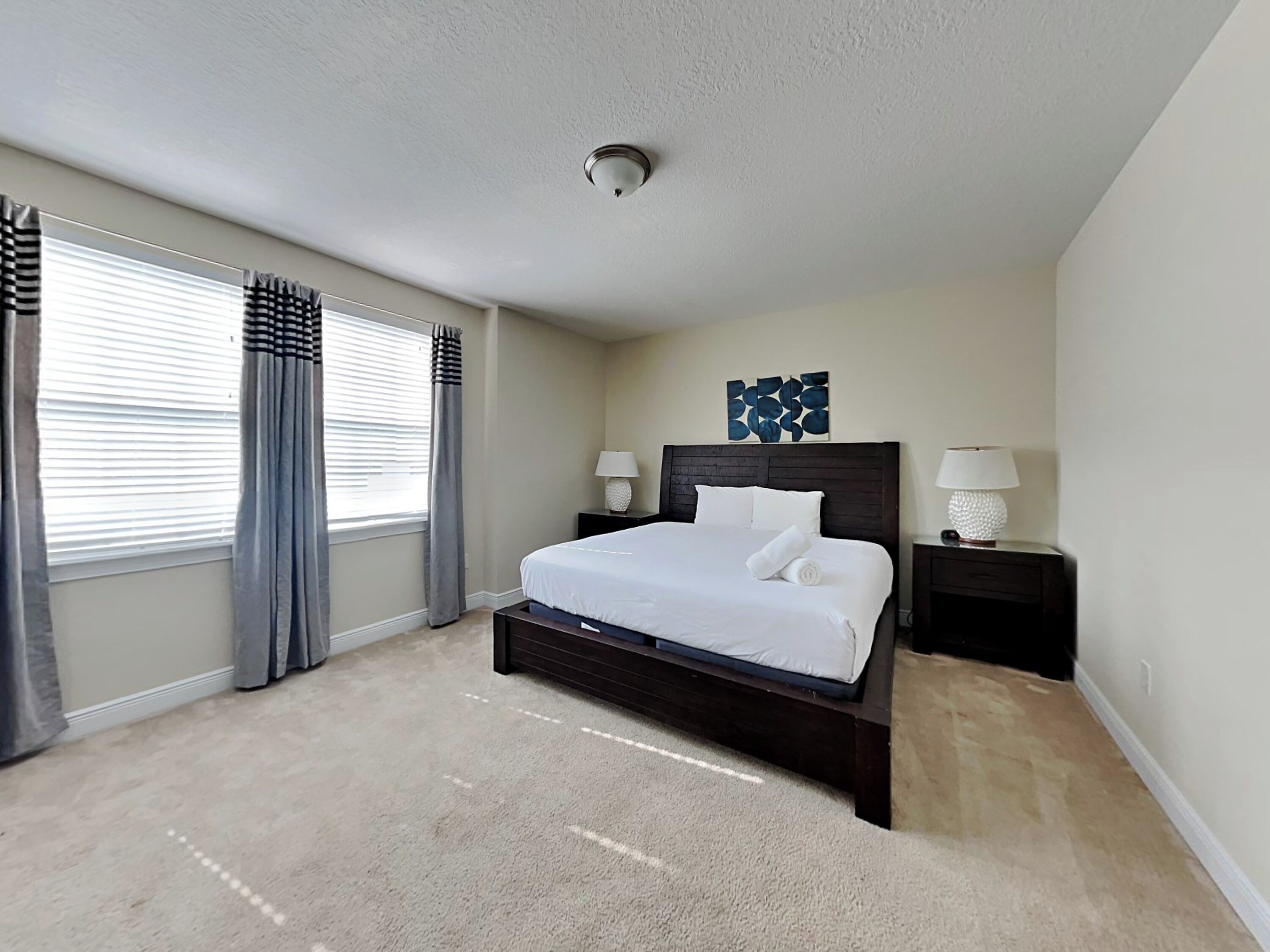 A bedroom with a large bed, two bedside tables with lamps, a ceiling light, and a window with curtains.
