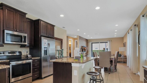 A modern kitchen with dark wood cabinets, stainless steel appliances, and a central island with stools. - 25% Off 8BR Villa! Pool/Spa.  Game & Movie Rooms (Davenport)