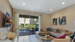 A spacious living room with a large sliding glass door leading to a patio area. There is a beige sofa, a coffee table, and two abstract paintings on the wall. - 25% Off 8BR Villa! Pool/Spa.  Game & Movie Rooms (Davenport)