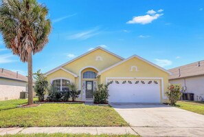 A single-story house with a garage, a front yard with a palm tree, and a clear blue sky. - 25% Off Indian Ridge Cozy Gem (Kissimmee)