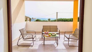 Un balcón con mesa y sillas dispuestas para dos, y vista al mar.