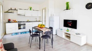 Una cocina moderna con armarios blancos, un comedor con mesa y sillas, un refrigerador y un televisor de pantalla plana montado en la pared.