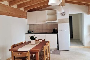 A modern kitchen with white cabinets, a wooden dining table, and a hanging light fixture. - Vinessa Apartment - Relaxation in the Heart of Toscolano (Provincia di Brescia)