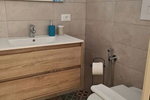 Et badeværelse med et trækommode, vask, toilet og brusebad.