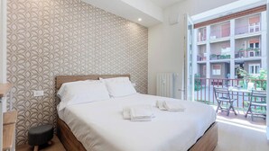 Ein Hotelzimmer mit einem Bett, einem kleinen Hocker, einer Heizung und einem Balkon mit Tisch und Stühlen.