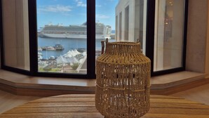 A wicker vase on a wooden table by a window with a view of a cruise ship docked at a marina. - Shell Living -Marina (FUNCHAL)