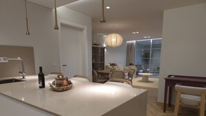 A modern kitchen with a central island, a dining area with a round table, and a seating arrangement. - Shell Living -Marina (FUNCHAL)