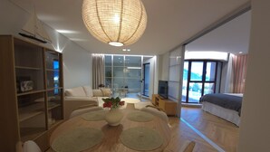 A modern living room with a round dining table, a sofa, a TV, and a large window. - Shell Living -Marina (FUNCHAL)
