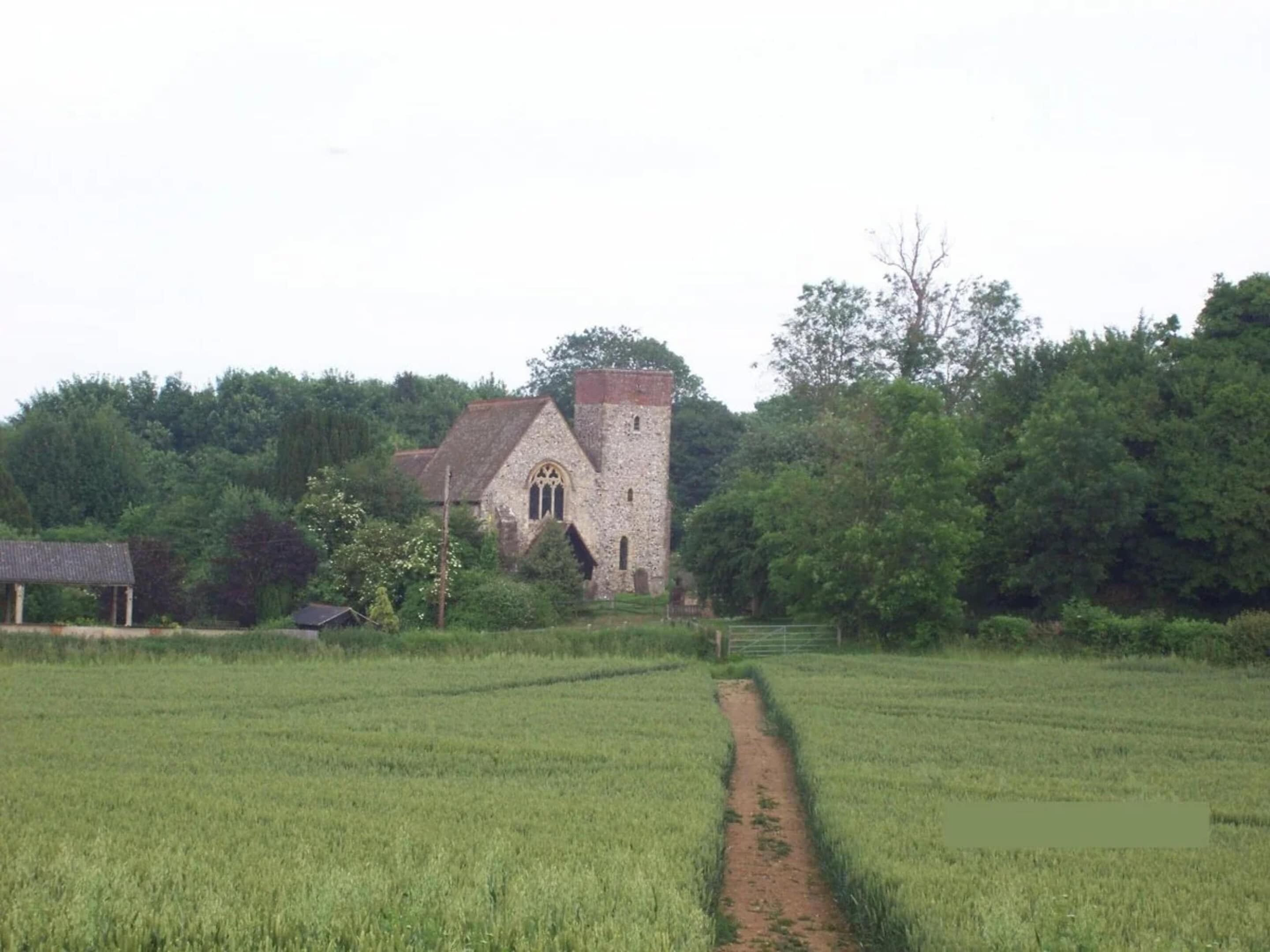 A stone church with a tower, surrounded by a green field and trees.