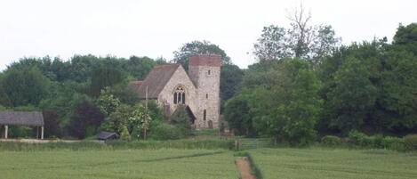 A stone church with a tower, surrounded by a green field and trees.