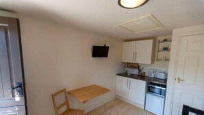 A compact kitchen with a wooden table and chair, white cabinets, a microwave, and a TV mounted on the wall. - Solo Country Getaway in Kent (Ashford)