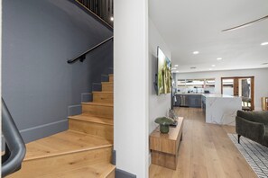 Een modern interieur met een houten trap, een keukenhoek en een zithoek met een bank.