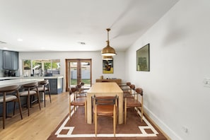A modern kitchen with a dining area, featuring a wooden table and chairs, a pendant light, and a view to the outside. - The Clubhouse Escape - sleeps 10! Movie theater, hot tub, pool, billiards! (Scottsdale)