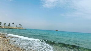 Ein Strand mit klarem türkisblauem Wasser, felsigem Ufer und einem entfernten Boot.