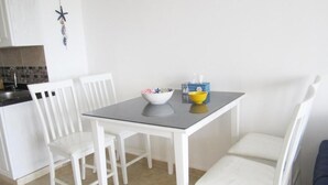 Ein kleiner Essbereich mit einem Tisch und vier weißen Stühlen. Auf dem Tisch stehen eine Schüssel und eine Dose.
