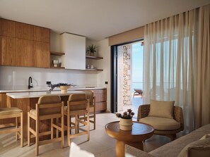 Eine moderne Küche mit Holzschränken, einer weißen Arbeitsplatte und einem Essbereich mit Holzsesseln. Ein runder Holztisch mit einer Blumenvase steht dort.